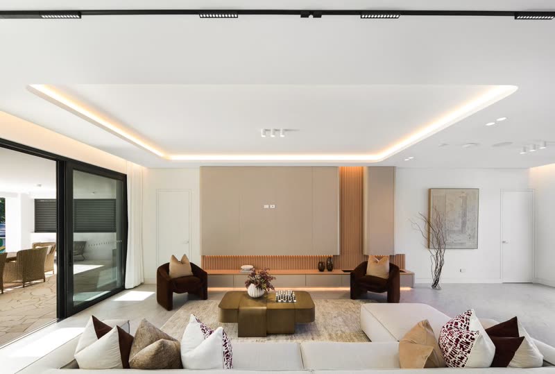 Large living room with a deep cream sectional sofa, a low olive coffee table, rust velvet armchairs and a recessed ceiling with warm lighting
