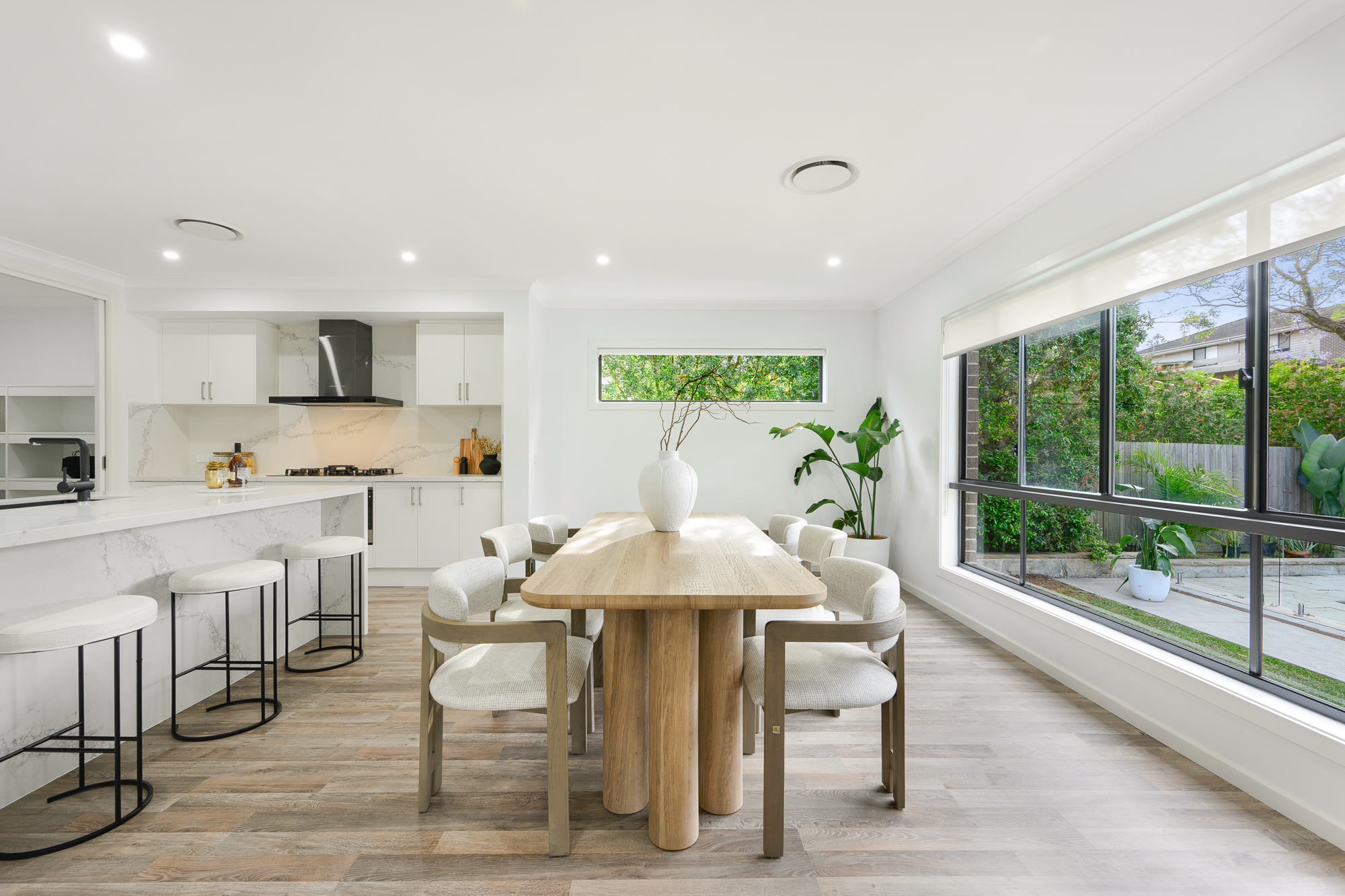 Bright kitchen and dining area with a light timber table, cream dining chairs and a large garden window