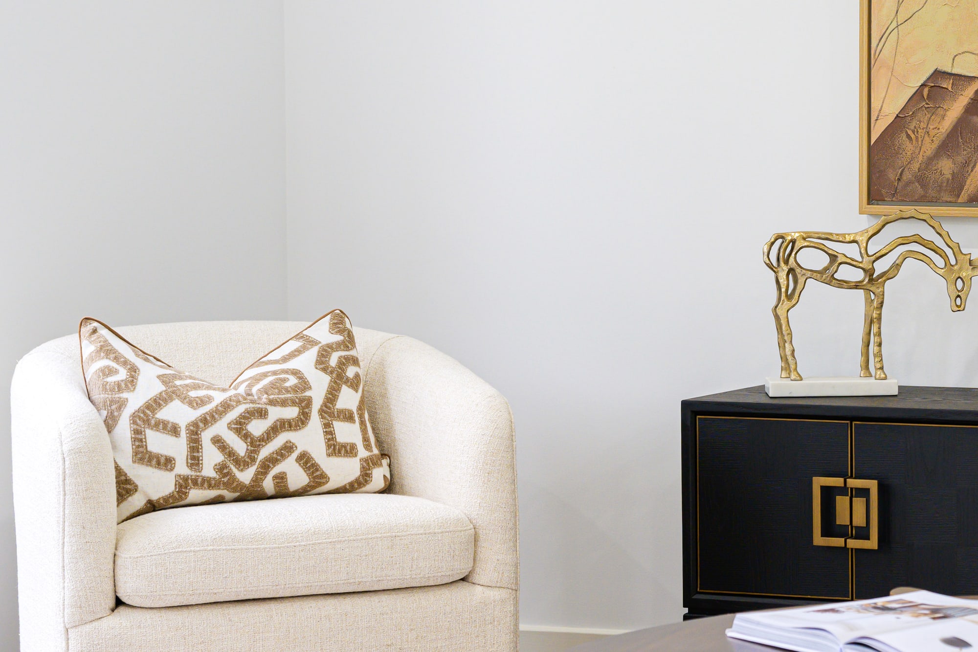 Cream swivel armchair with a patterned cushion beside a gold horse sculpture