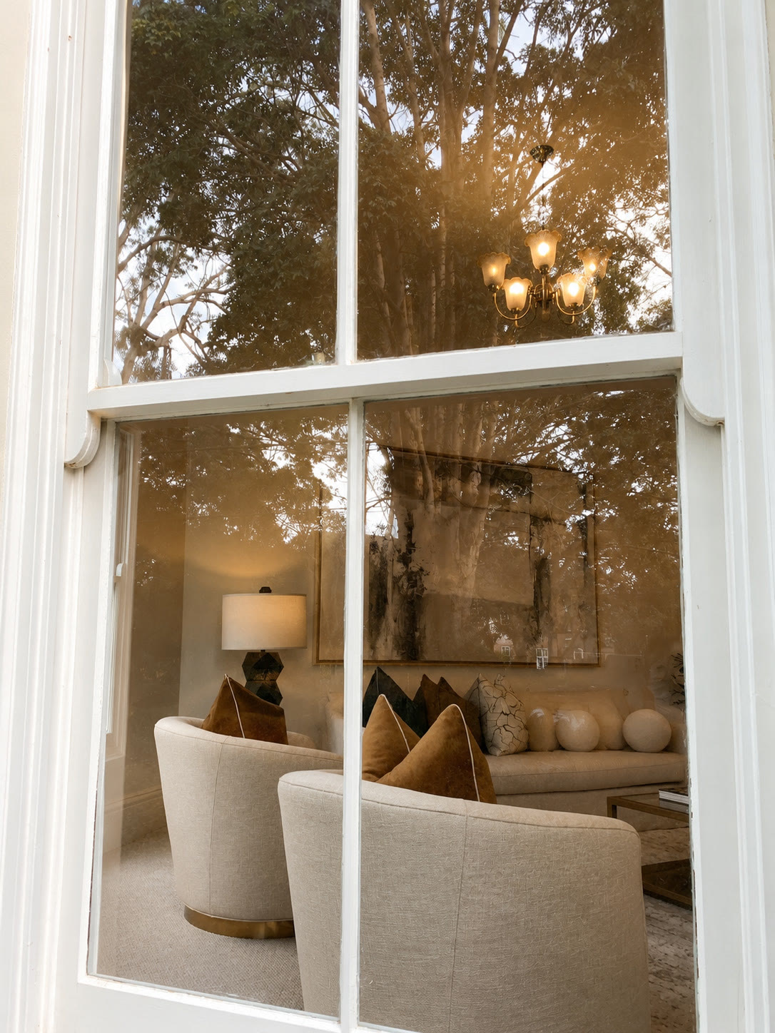 View through a sash window to cream armchairs and a sofa in the living room