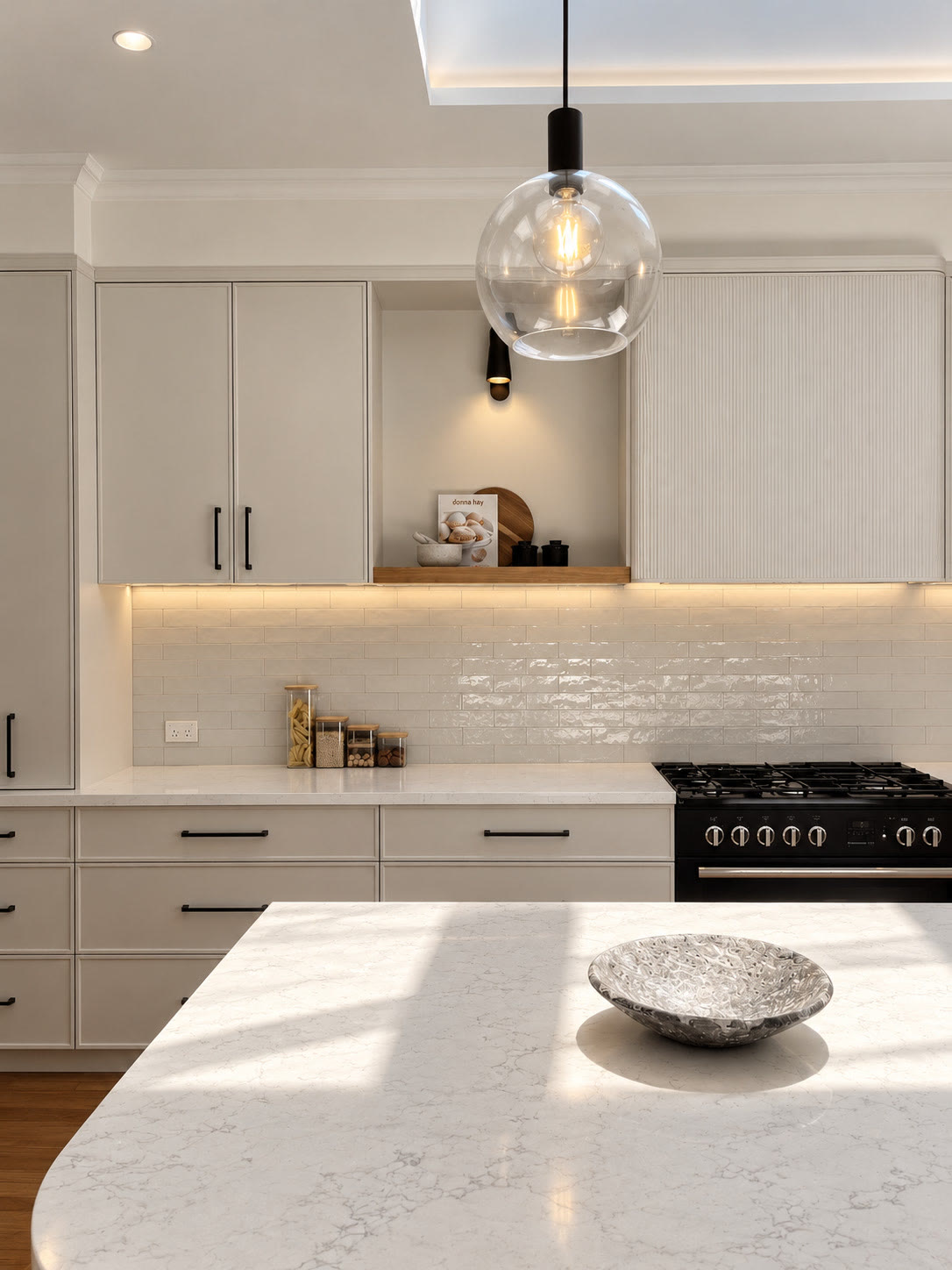 Kitchen with a marble island, pale cabinetry with black handles, a glass globe pendant and a range cooker