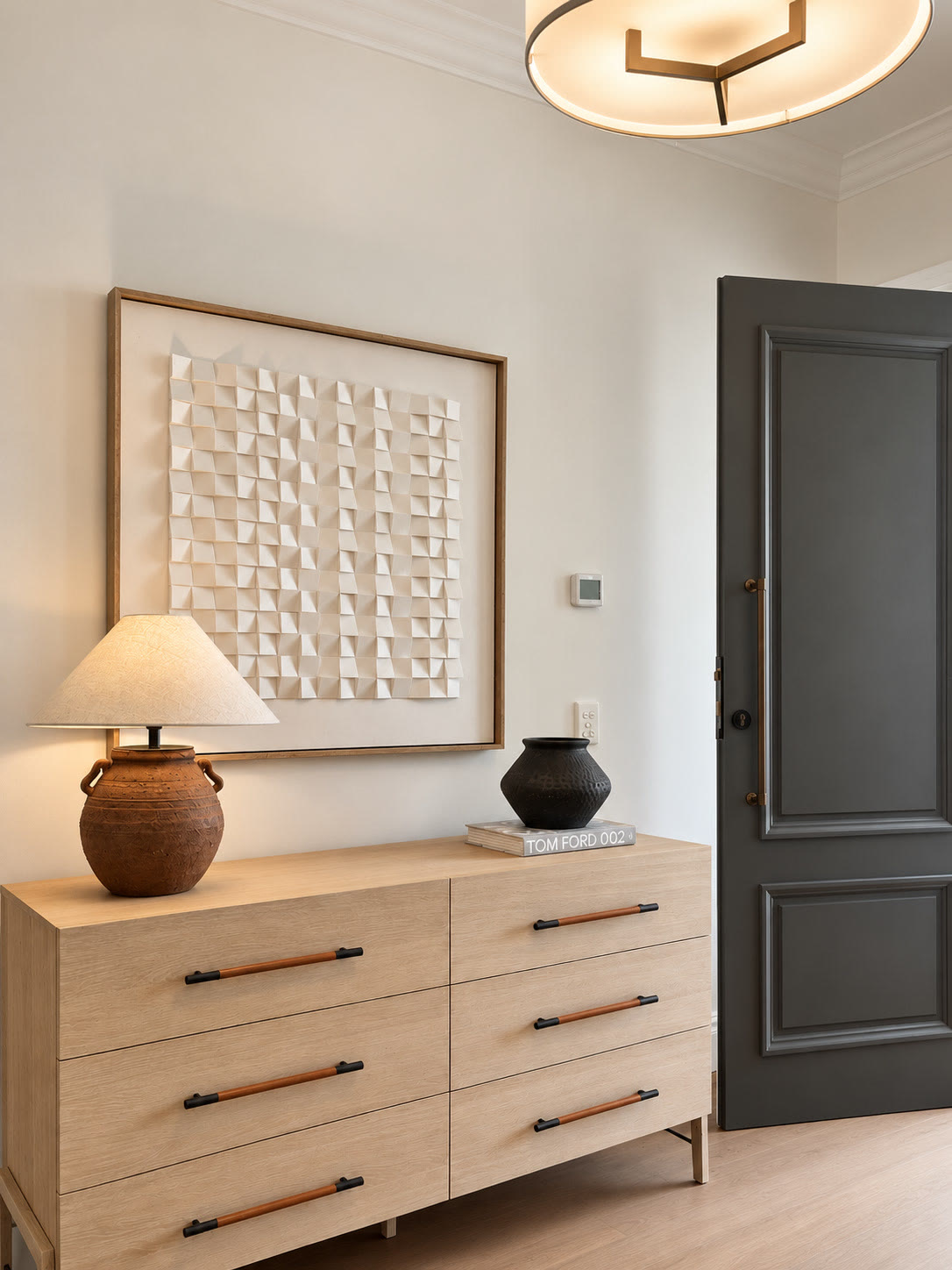 Entry with a pale timber chest of drawers, a terracotta lamp, a textured framed artwork and a charcoal door