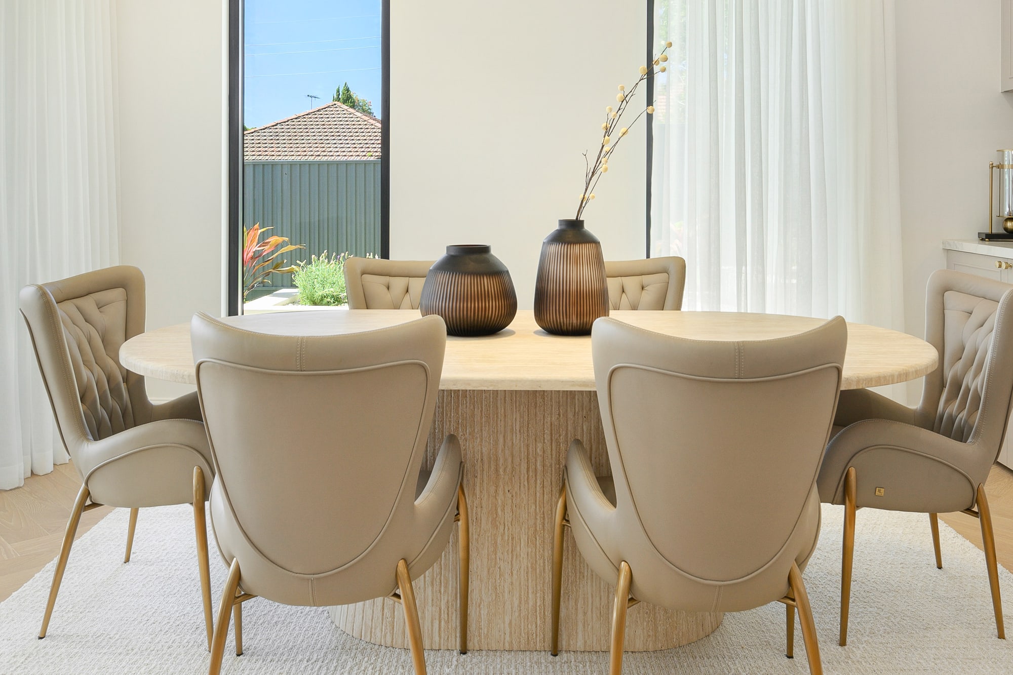 Round pedestal dining table with beige upholstered chairs and a pair of dark vases as a centrepiece