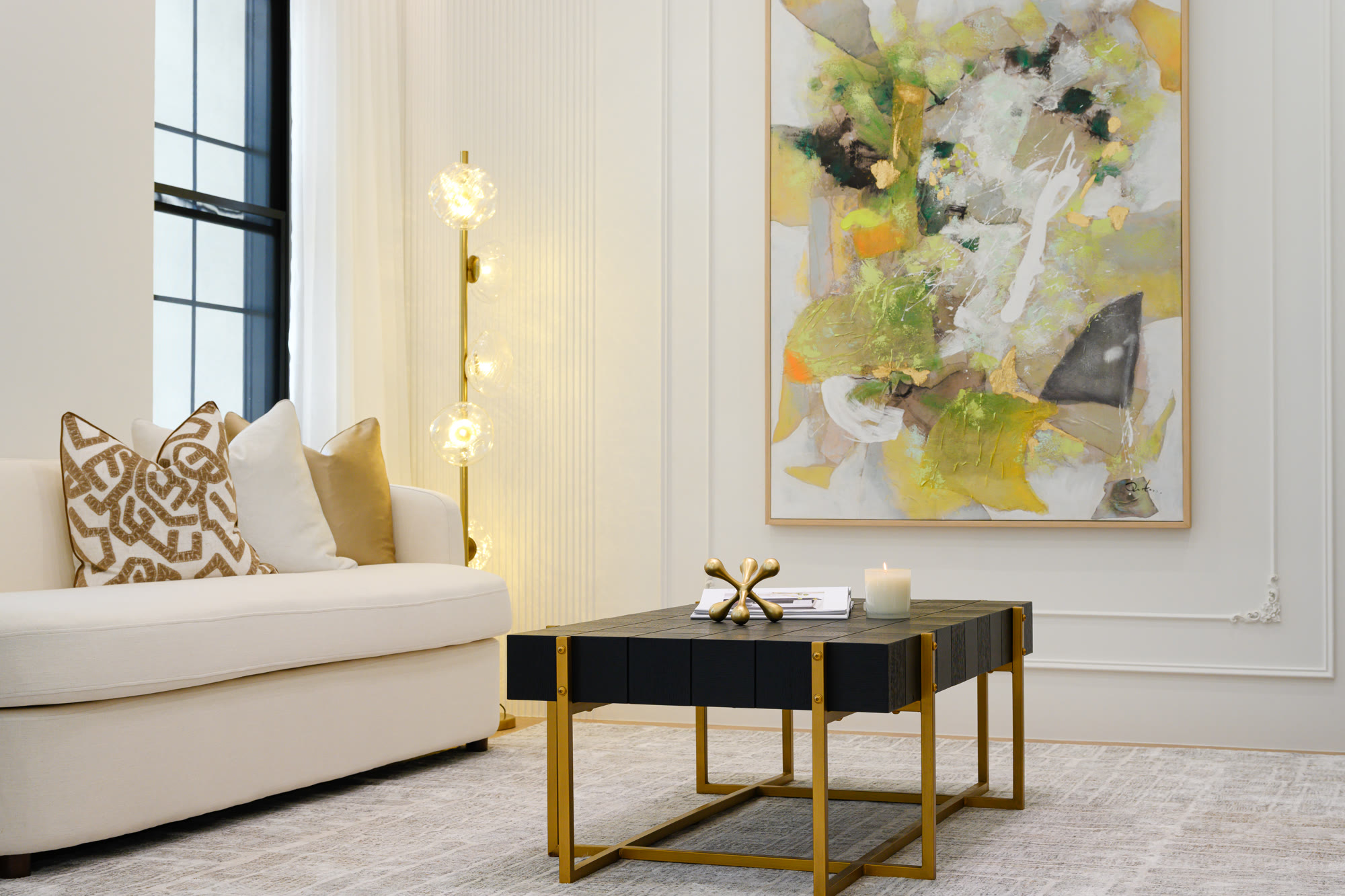Living room corner with a curved cream sofa, a black and gold coffee table and a large abstract painting