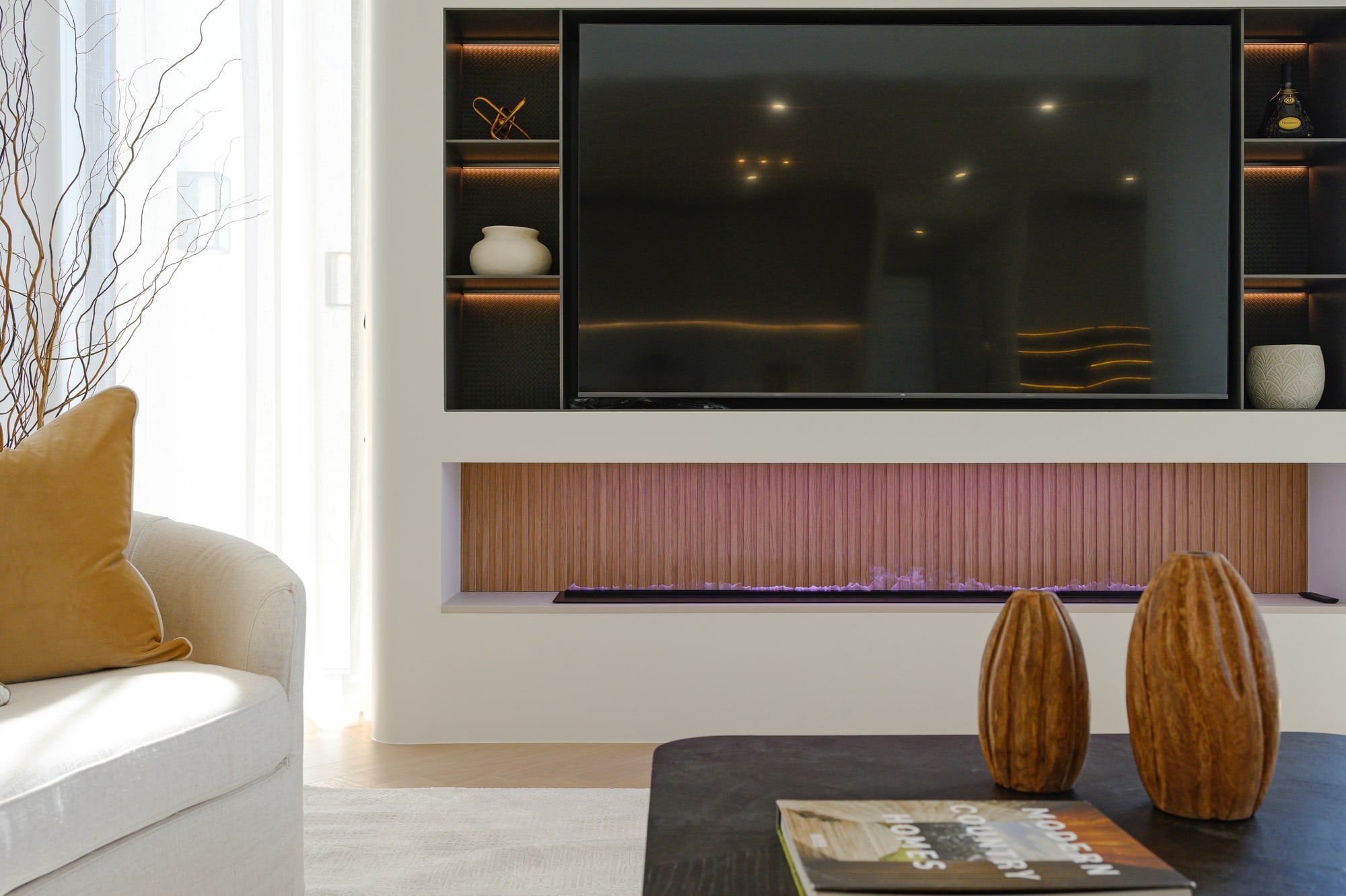 Feature wall with a built-in television and fireplace, wooden vases and a cream sofa with mustard cushions