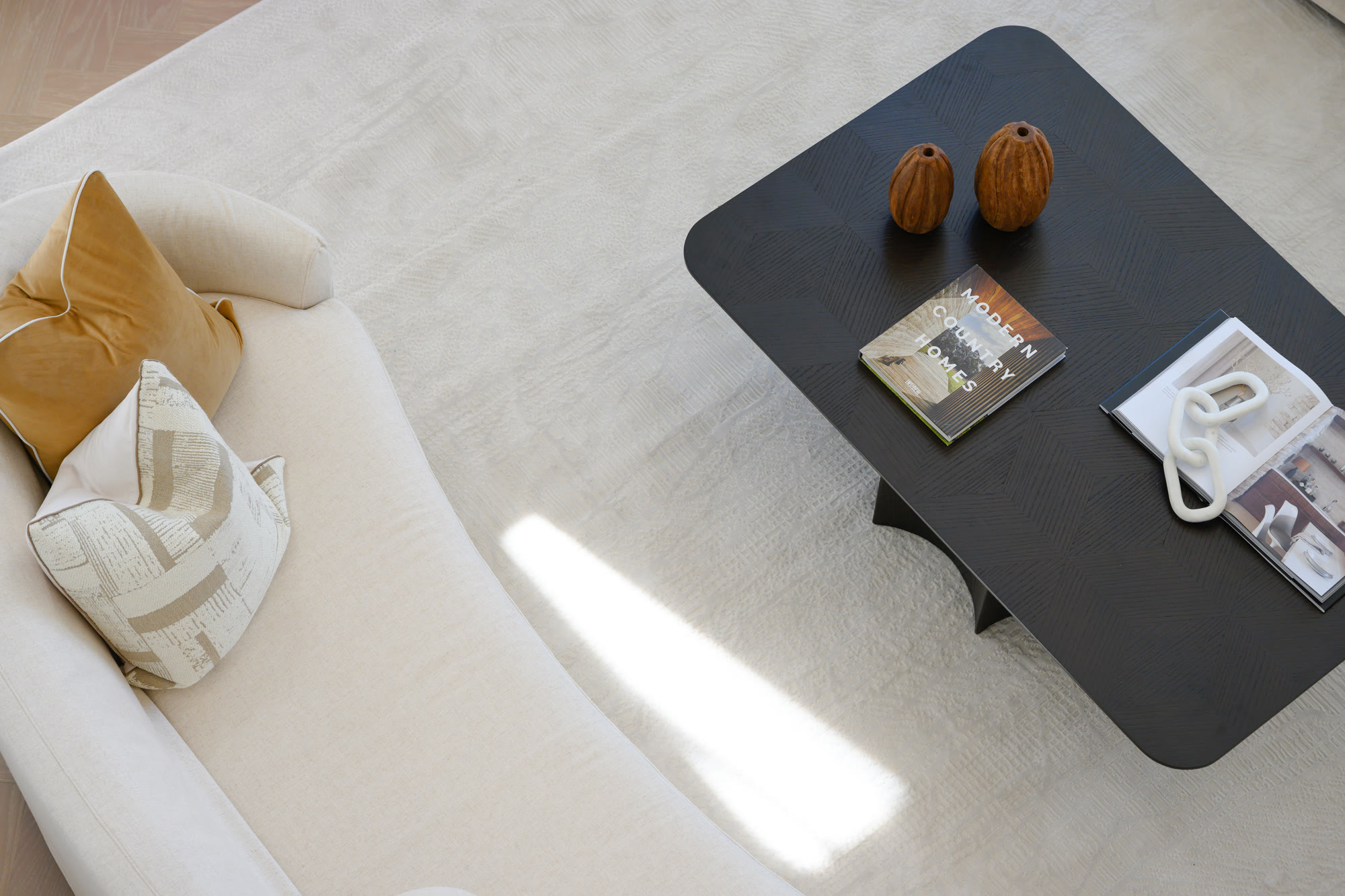 Close view of a cream sofa with mustard and patterned cushions beside a black coffee table styled with books and wooden vases