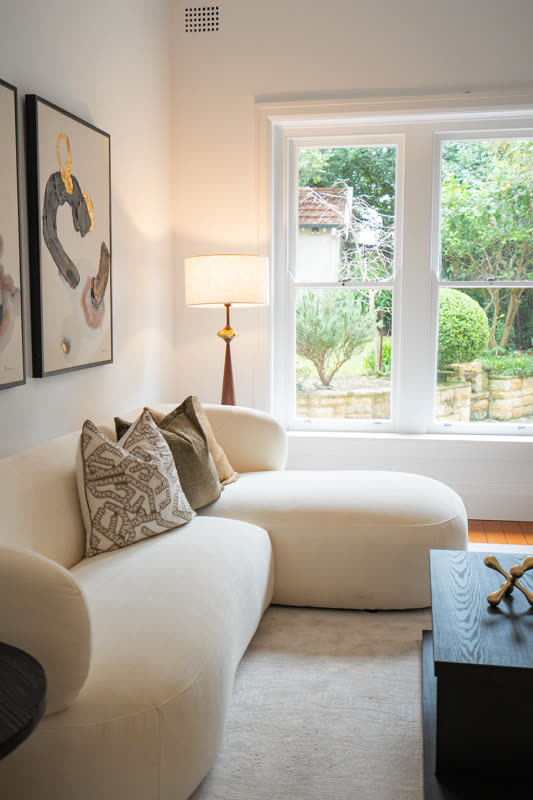 Living room with a curved cream sofa, abstract artwork and a window to the garden