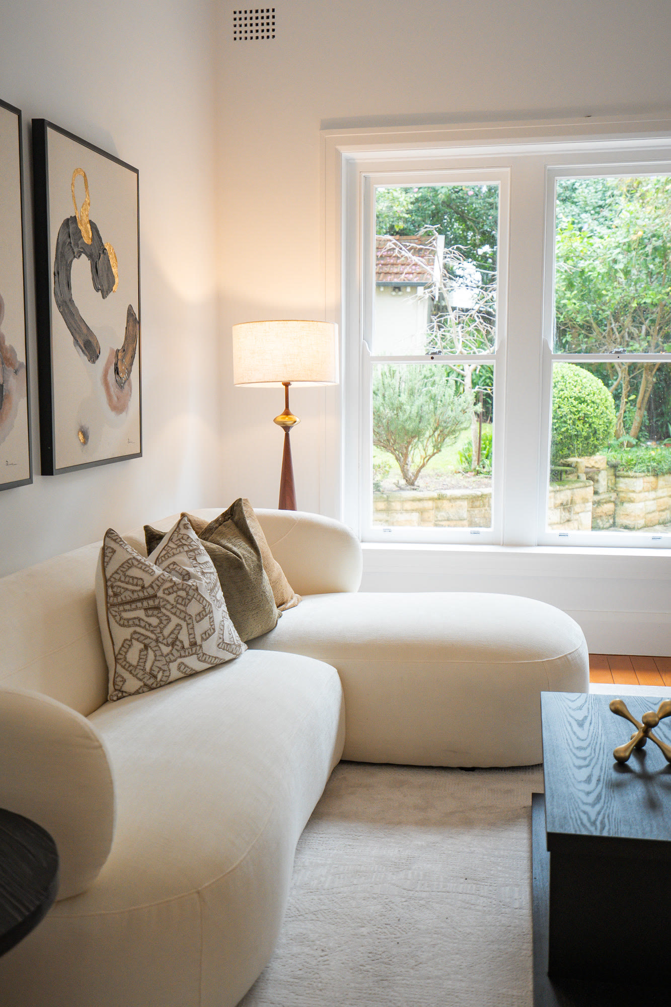 Living room with a curved cream sofa, abstract artwork and a window to the garden