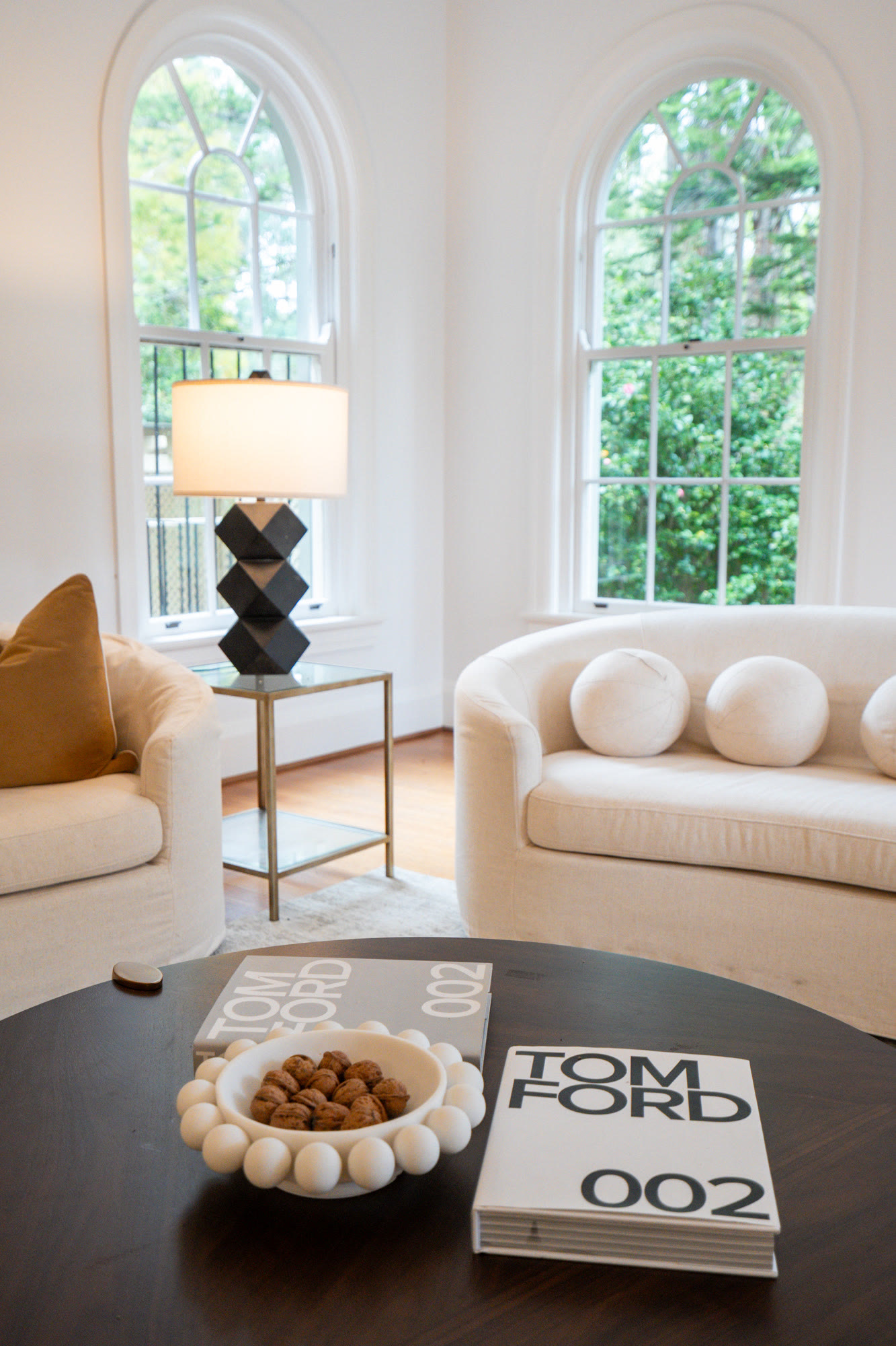 Living room with arched windows, a curved cream sofa with round cushions, a black lamp and a round dark coffee table