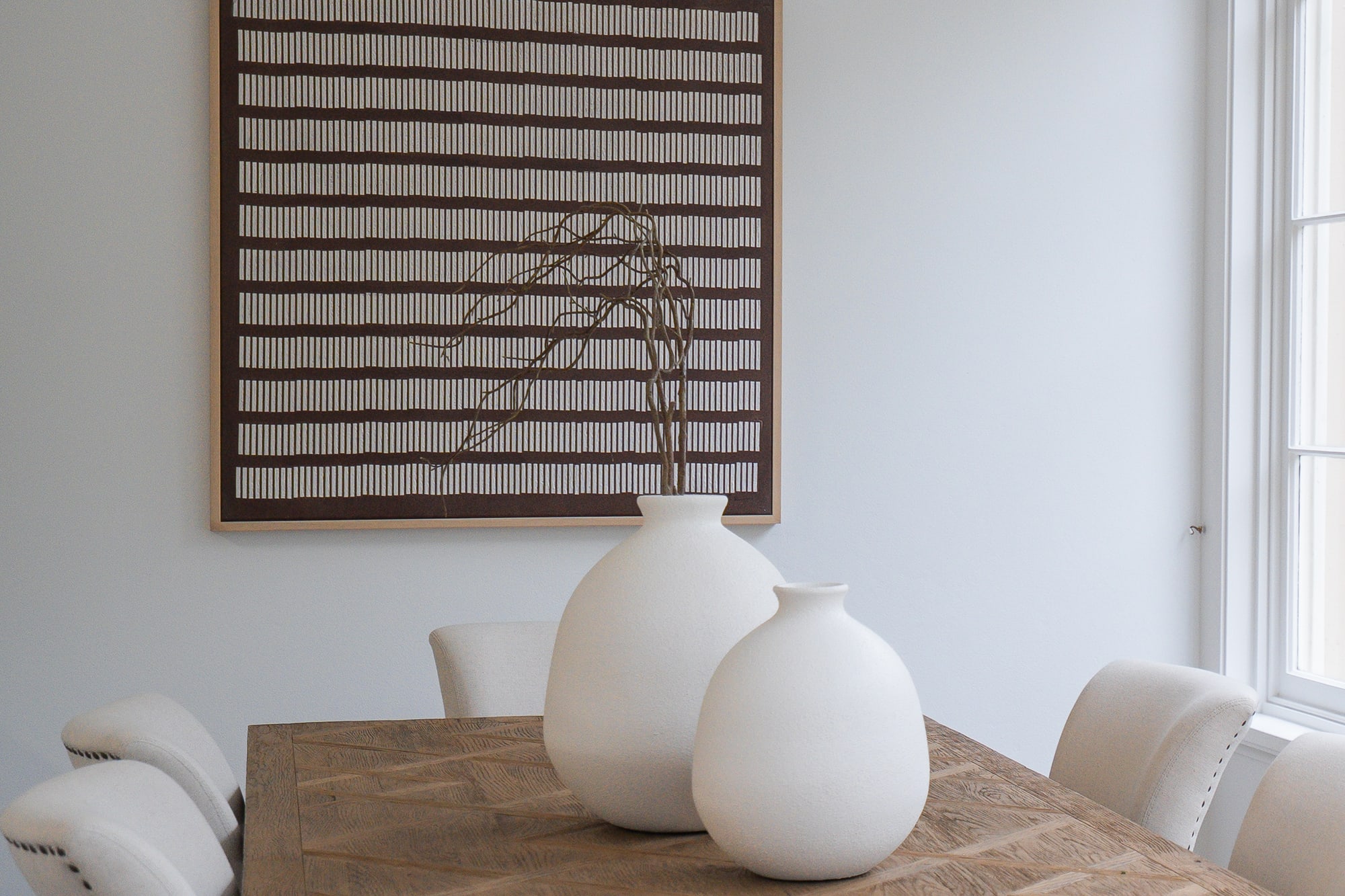 Framed striped artwork above a dining table styled with white vases