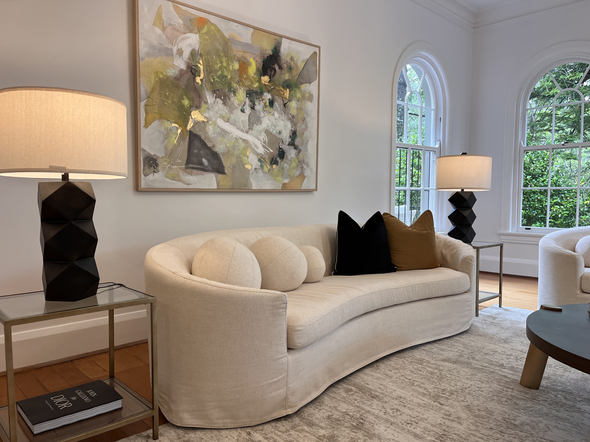 Curved cream sofa with black and tan cushions, a black faceted lamp and a large abstract painting