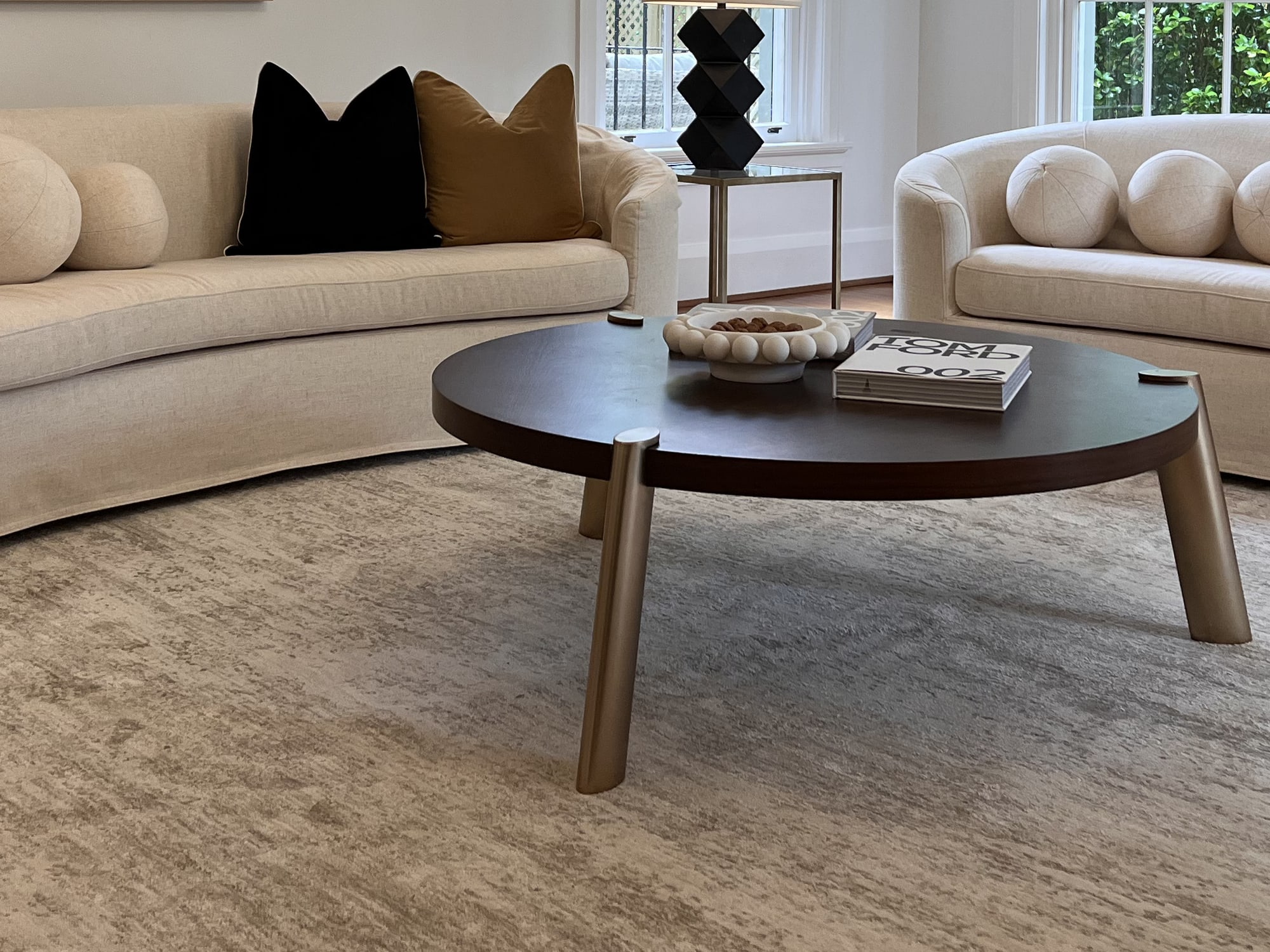 Round dark coffee table with a book and cushions on a curved cream sofa