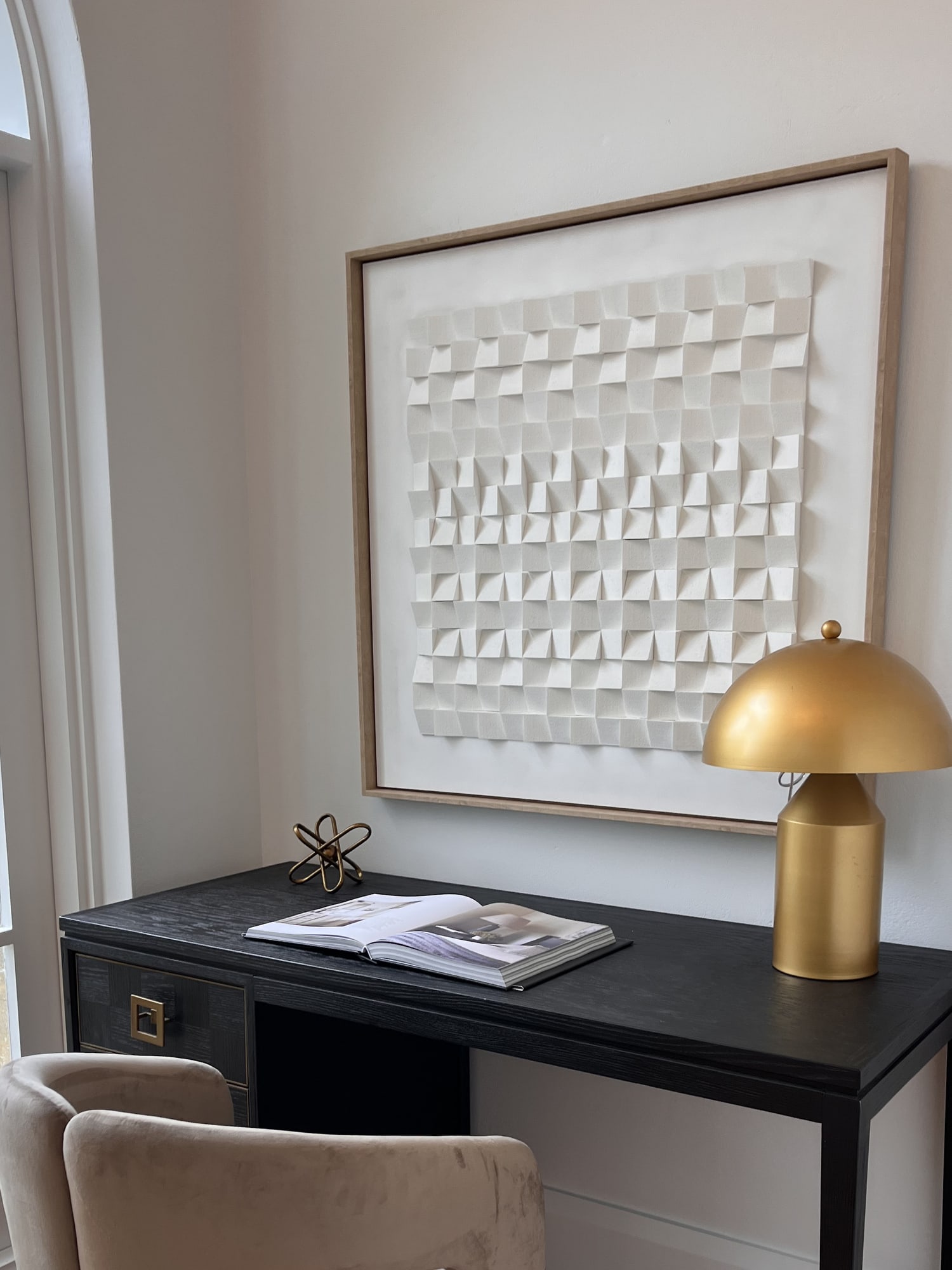 Black writing desk with a gold dome lamp and a textured white artwork