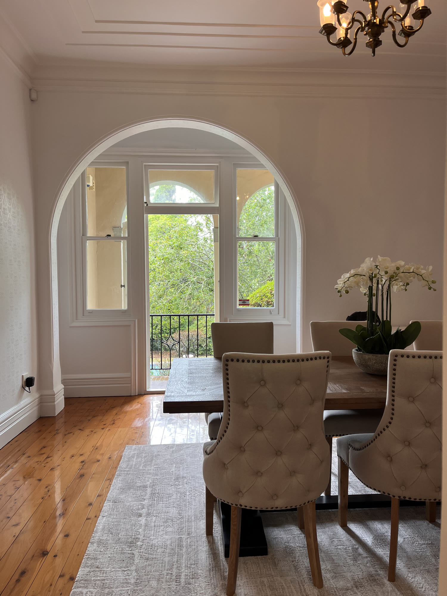 Dining room with tufted cream chairs, a dark table and an arched French door onto a balcony