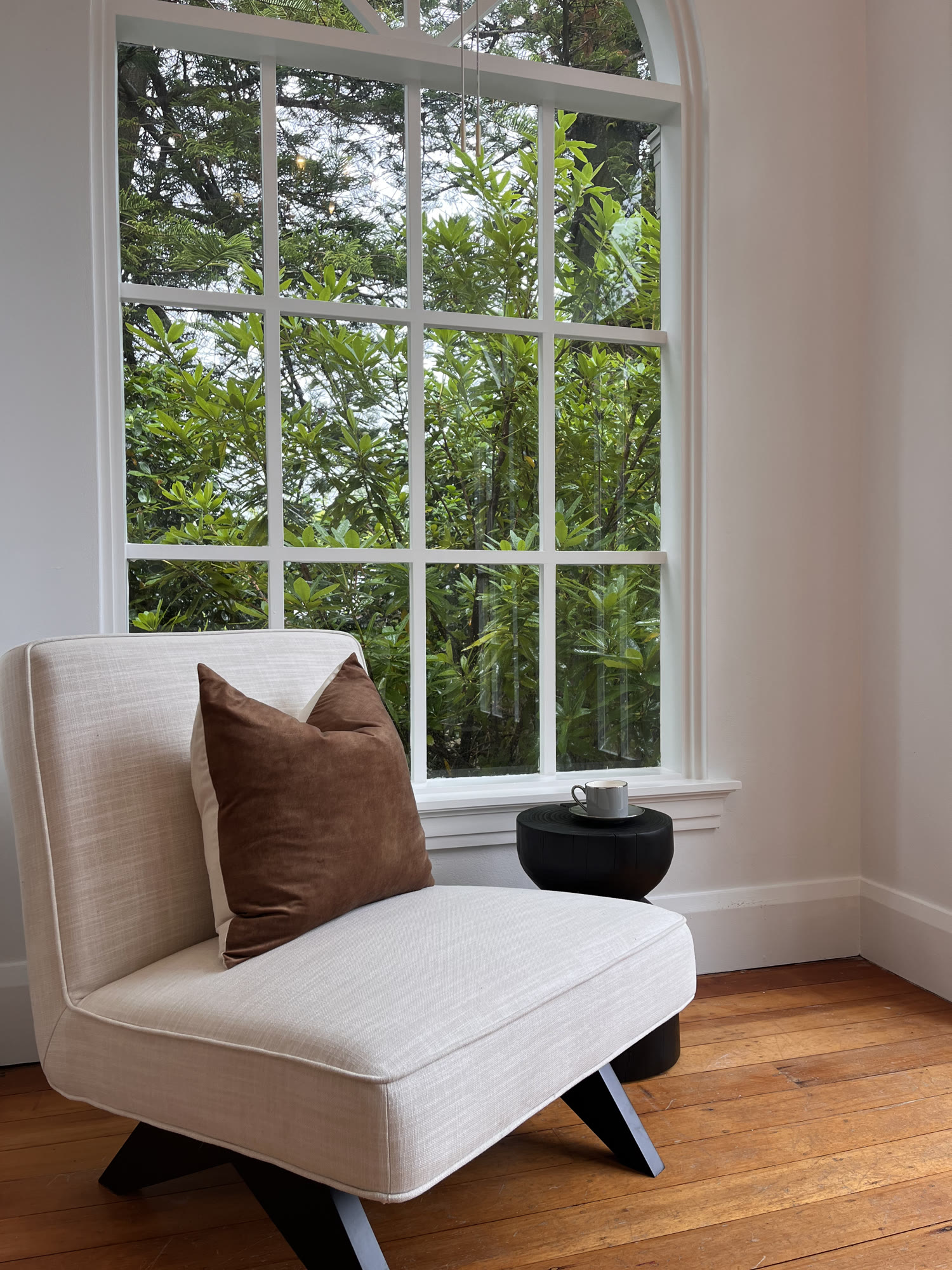 Cream accent chair with a tan cushion beside a tall window