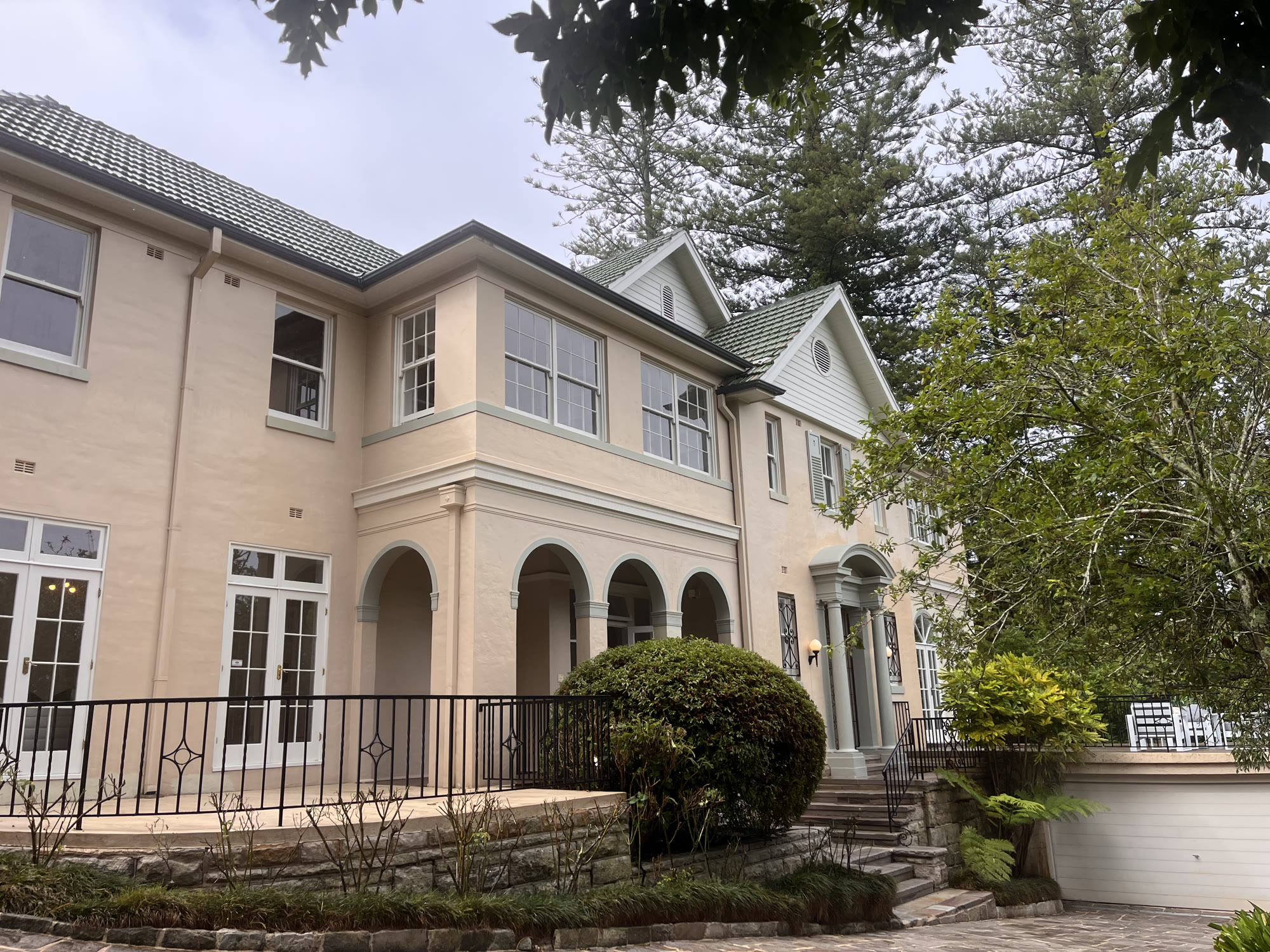 Two-storey house with arched openings, a stone terrace and mature trees