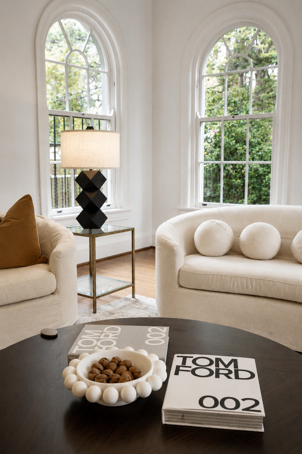 Round dark coffee table with a bowl of wooden beads and a book, with arched windows beyond