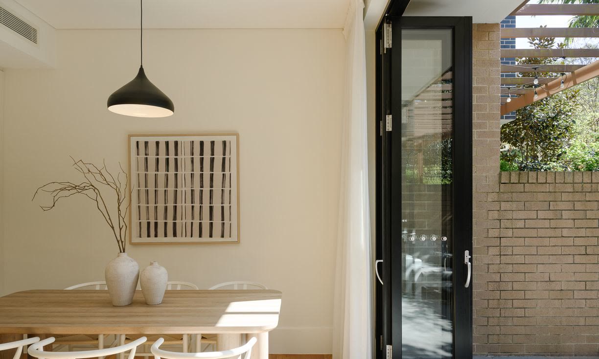 Dining area with a timber table, white wishbone chairs, a black pendant light and bi-fold doors to the courtyard