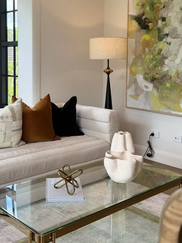 Cream sofa cushions beside a glass coffee table styled with a sculpture and books