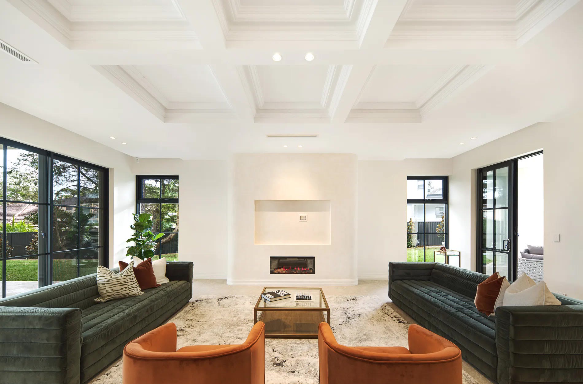 Open-plan living room with deep green channelled sofas, rust velvet armchairs and a coffered ceiling