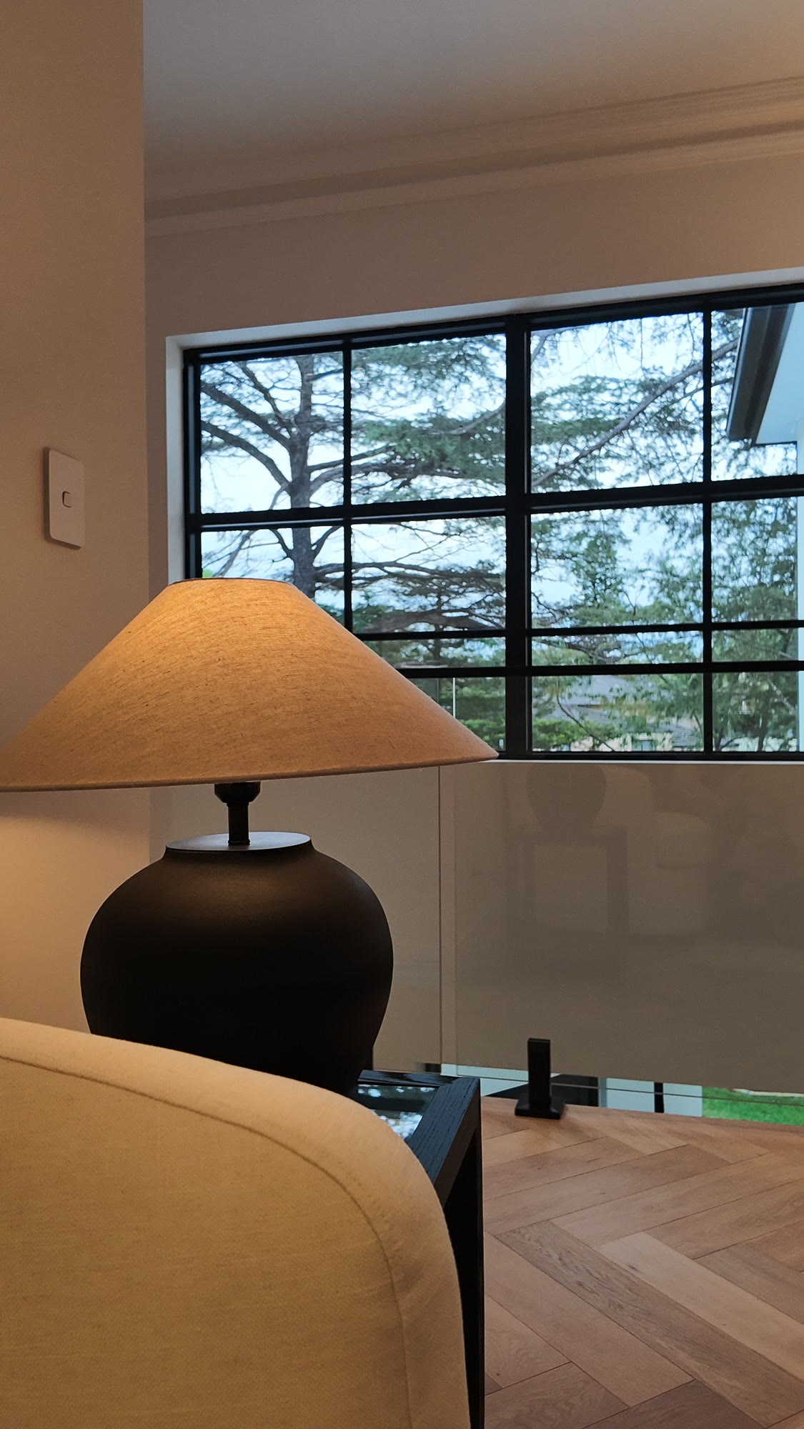 Table lamp with a black base beside a black-framed window above a herringbone timber floor