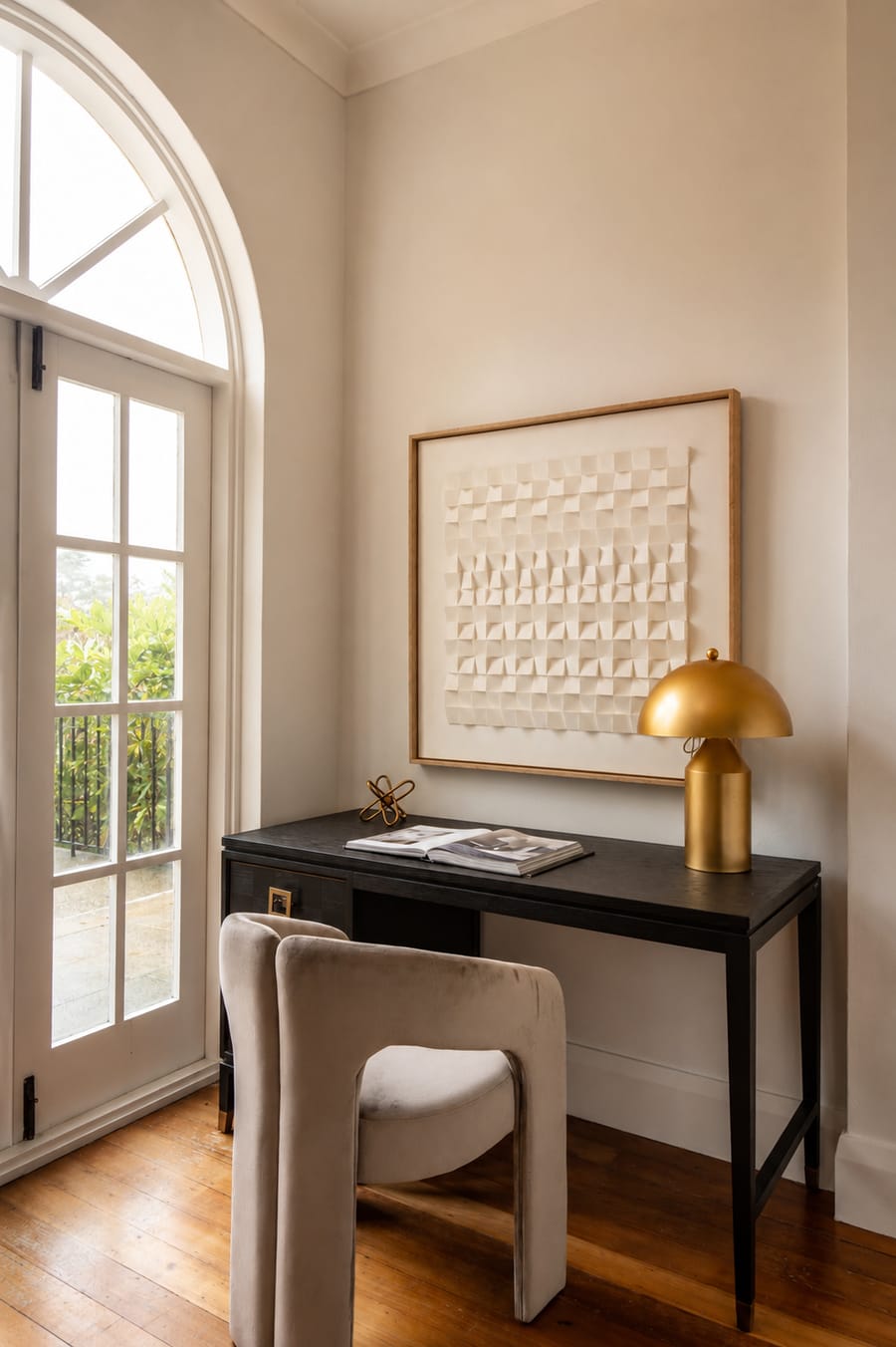Study nook with a black desk and gold lamp beside an arched door